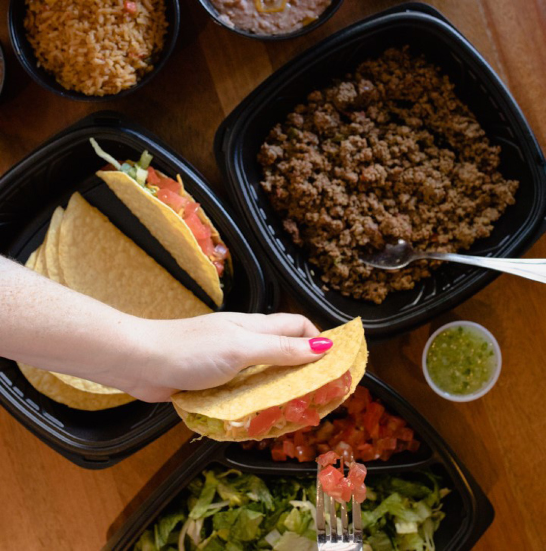 A hand holding a taco, surrounded by various taco ingredients